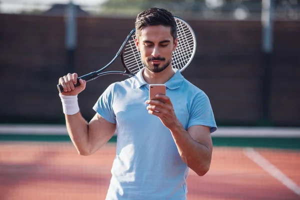 Bonito Homem Está Usando Telefone Inteligente Enquanto Joga Tênis Campo — Fotografia de Stock