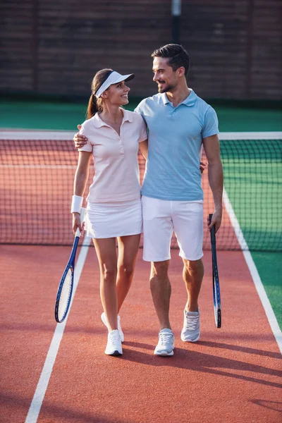 ハンサムな男性と美しい女性を抱き締めると 試合後屋外テニスコートに立って笑顔 — ストック写真