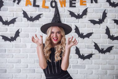 Güzel sarışın kız siyah elbise ve cadı şapka pençeleri gösterilen, kameraya bakıyor ve Cadılar Bayramı için dekore edilmiş arka plan üzerinde gülümseyen