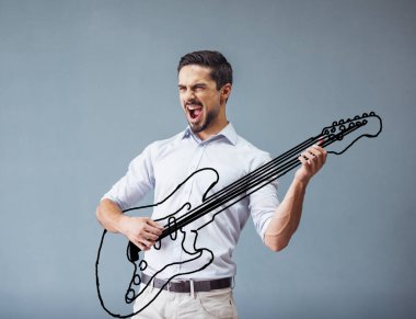 Yakışıklı, sıradan kıyafetler ve güneş gözlüğü takmış genç bir adam gri arka planda gitar çalıp şarkı söylüyor.