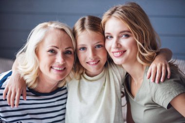 Güzel kadınlar Üretimi: anneanne, anne ve kızı sarılma, kameraya bakıyor ve evde kanepede otururken gülümseyen