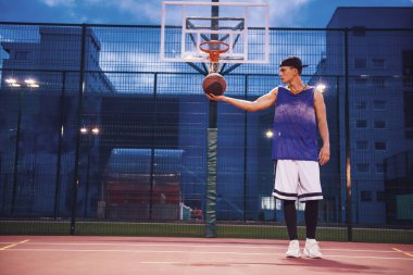 Şık genç basketbolcu akşamları açık havada bir top basketbol sahası üzerinde kap ayakta tam uzunlukta portresi