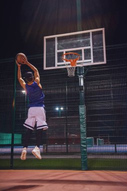 Şık genç basketbolcu atlama ve açık havada geceleri oynarken bir topu delikten çekim kap tam uzunlukta portresi