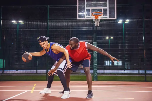 Handsome guys are playing basketball outdoors at night