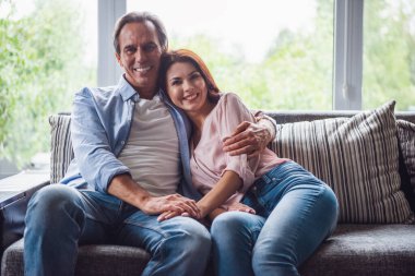 Güzel çift sarılma, kameraya bakıyor ve evde kanepede istirahat ederken gülümseyen