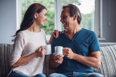 Güzel çift bardak holding, birbirine bakarak ve evde kanepede istirahat ederken gülümseyen