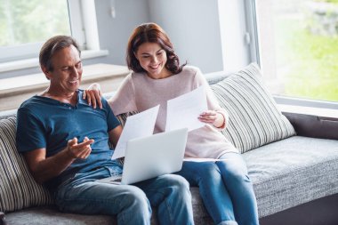 Güzel çift bir dizüstü bilgisayar kullanarak, belgeleri eğitim ve evde kanepede çalışırken gülümseyen