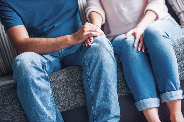 Cropped image of beautiful couple holding hands while resting on couch at home