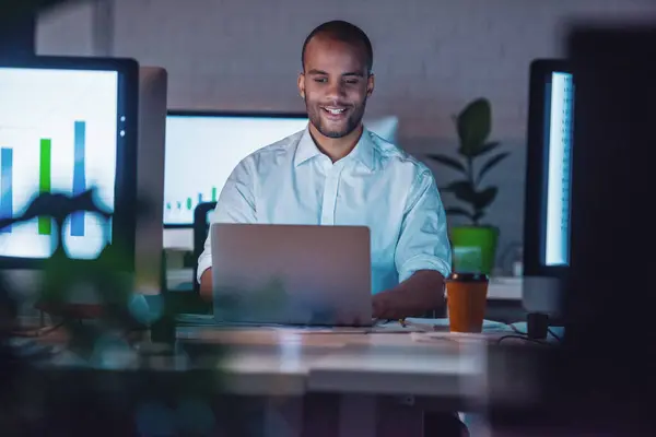 Handsome Afro American businessman in classic suit is using a laptop and smiling while working in office late at night
