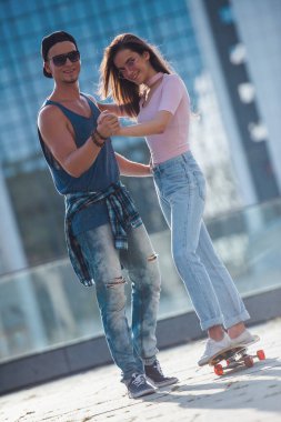 Şık genç çift zaman şehirde birlikte geçiriyor. Adam sevgilisini kaykay öğretiyor