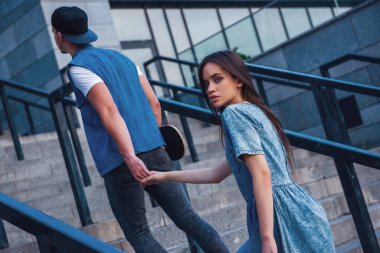 Şık genç çift açık havada yürürken el ele tutuşarak, adam bir kaykay tutuyor