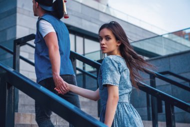 Şık genç çift açık havada yürürken el ele tutuşarak, adam bir kaykay tutuyor