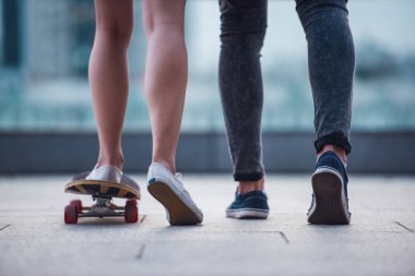 Şehirde birlikte vakit şık genç çift kırpılmış. Adam sevgilisini kaykay öğretiyor