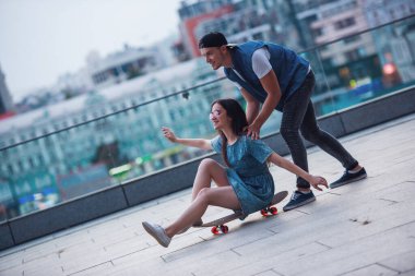 Genç çift açık havada eğleniyor, adam kız arkadaşı bir kaykay üzerinde bastırıyor