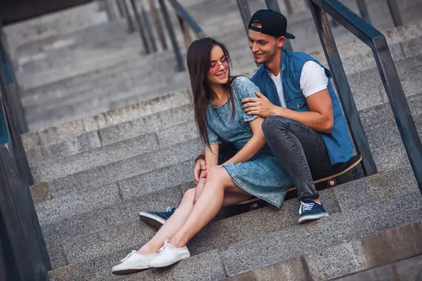 Şık genç çift sarılma, söz ve kaykay merdiven üzerinde otururken gülümseyen