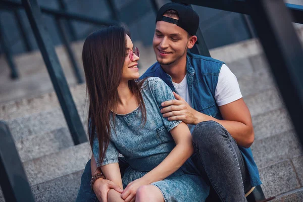 Şık genç çift sarılma, söz ve merdivenlerde otururken gülümseyen