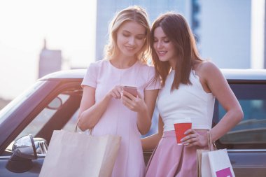 Güzel kızlar alışveriş torbaları ile bir akıllı telefon kullanarak, söz ve arabalarını yakın dururken gülümseyen