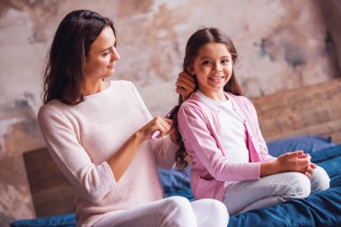 Güzel anne ve kızı yatağa evde otururken gülümsüyor musun, anne kızının saç tarama