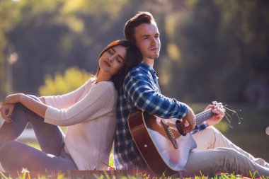 Güzel genç çift ekose Park üzerinde dinlenme süre gülümsüyor, adam gitar çalıyor