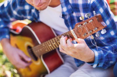 Yakışıklı genç adamın parkta oturan süre gitar çalmak kırpılmış görüntü