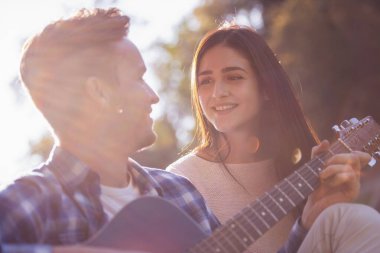 Güzel genç çift şarkı ve bir ekose parkta, istirahat sırasında gülümseyen adam gitar çalıyor