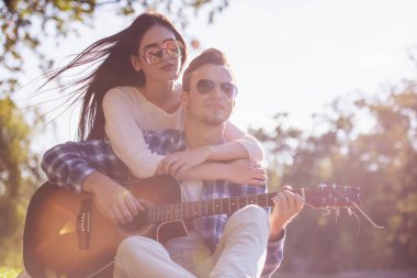 Güzel genç çift sarılma ve parkta oturan gülümsüyor, adam gitar çalıyor
