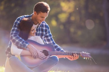 Güzel genç çift ekose parkta dinleniyor, adam kız arkadaşı gitar çalmayı öğretiyor