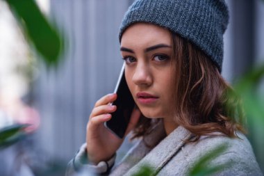 Güzel kız ceket ve kapağı açık havada duran süre cep telefonla konuşuyor