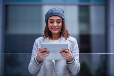 Güzel kız ceket ve kap dijital tablet kullanma ve açık havada dinlenme süre gülümseyen