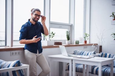 Şık genç işadamı uzun siyah saçlı bir smartphone kullanarak ve kafede çalışırken gülümseyen