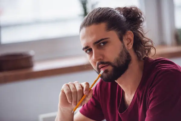 Bir Kalem Tutan Kameraya Bakarak Uzun Siyah Saçlı Yakışıklı Genç — Stok fotoğraf
