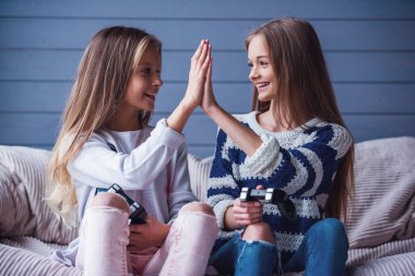 İki çekici genç kız rahat kıyafetler içinde video oyun konsolunda oynamak, çak bir beşlik veren ve evde kanepede otururken gülümseyen