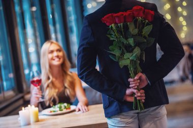 Güzel kız restoranda masada oturan ve bir adam onun arkasından gül tutarken gülümseyen