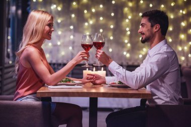 Güzel genç çift birbirine bakarak, birlikte kadeh şarap tungur ve onların Tarih sırasında bir restoranda gülümseyen