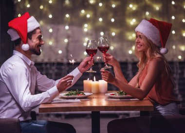 Noel Baba şapkaları güzel genç çift birbirine bakarak, birlikte kadeh şarap tungur ve süre kutlama yeni yıl bir restoranda gülümseyen