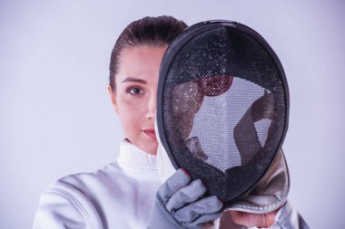 Koruyucu giyim güzel kadın fencer maske tutarak ve gri arka plan üzerinde kamera bakıyor
