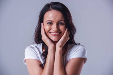 Çekici genç kadın kameraya bakarak ve gri arka plan üzerinde gülümseyen