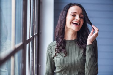 Çekici genç kadın saçları ile oynama ve odasında dururken gülüyor