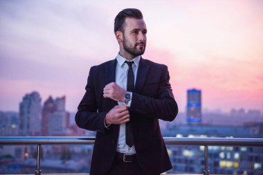 Takım elbiseli yakışıklı işadamı Balkonda duran, onun arkasında güzel gün batımı sırasında onun kol düğmeleri uyum sağlıyor.
