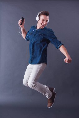 Yakışıklı delikanlı kulaklık müzik ve gri arka plan üzerinde atlama sırasında şarkı