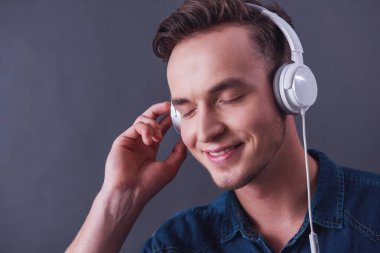 Kulaklığımda yakışıklı genç gri arka plan üzerinde müzik dinleme