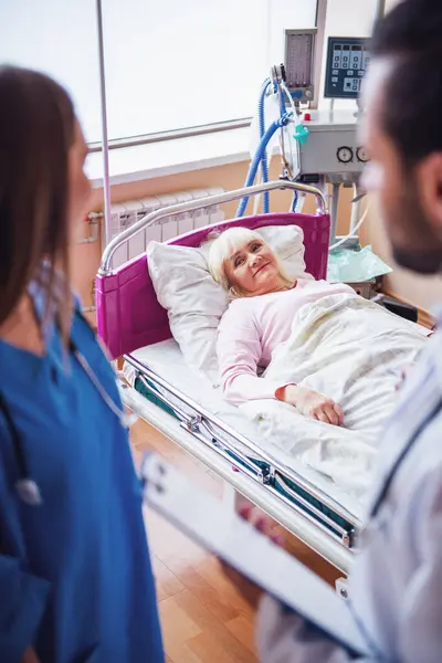 老妇人躺在床上微笑着 在医院病房 护士和医生看着她 免版税图库图片