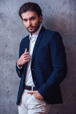 Yakışıklı emin işadamı ile kıl, takım elbise, gri arka plan üzerinde kamera bakıyor