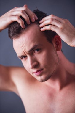 Yakışıklı genç çıplak gövde ile saçları incelenmesi ve gri arka plan üzerinde kamera bakıyor