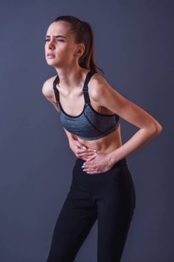 Spor giyim güzel kız mide duygu acısını gri arka plan üzerine dokunuyor