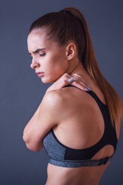 Güzel kızı spor giyim gri arka plan üzerinde omuz duygu acısını dokunuyor