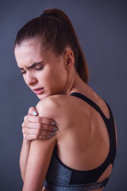 Güzel kızı spor giyim gri arka plan üzerinde omuz duygu acısını dokunuyor