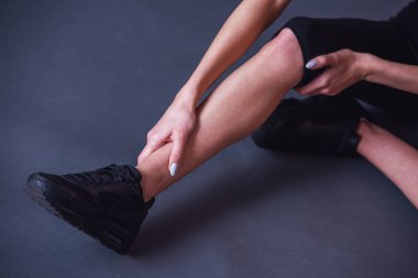 Kız yerde gri arka plan üzerinde otururken bacak duygu acısını dokunmadan spor giyim görüntü kırpılmış