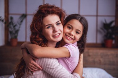 Güzel anne ve sevimli kızı sarılma, kameraya bakıyor ve birlikte evde vakit ise gülümseyen