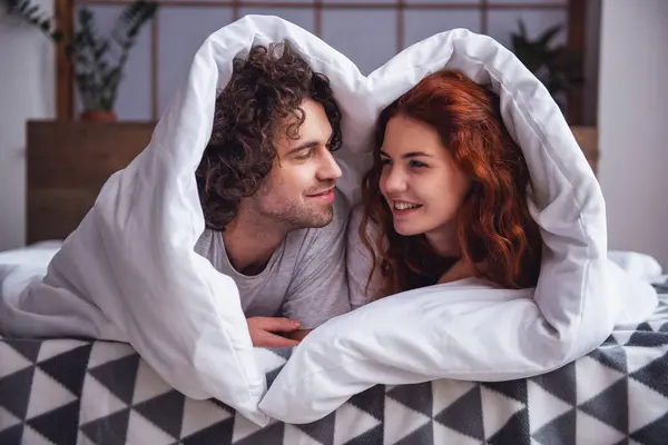 美しいカップルが話していると 毛布で包みながらベッドで横になっている笑顔 ストック画像